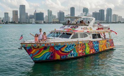 Colorful family-friendly yacht with joyful passengers sailing in Miami, showcasing vibrant designs and city skyline in the background.