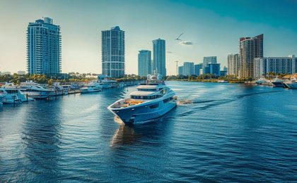 a luxurious yacht glides through the shimmering waters of fort lauderdale's bustling marina, surrounded by sleek high-rise buildings and vibrant city life under a clear blue sky.